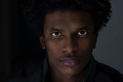 Face 5. Horizontal color close-up of a man looking directly at the camera, with low-key indoor night