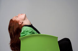 Side profile color fashion photo of a redheaded woman sitting on a lime green chair, head tilted bac
