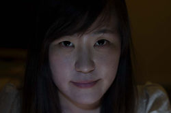 Face 7. Horizontal color close-up of a man looking directly at the camera, with low-key indoor night