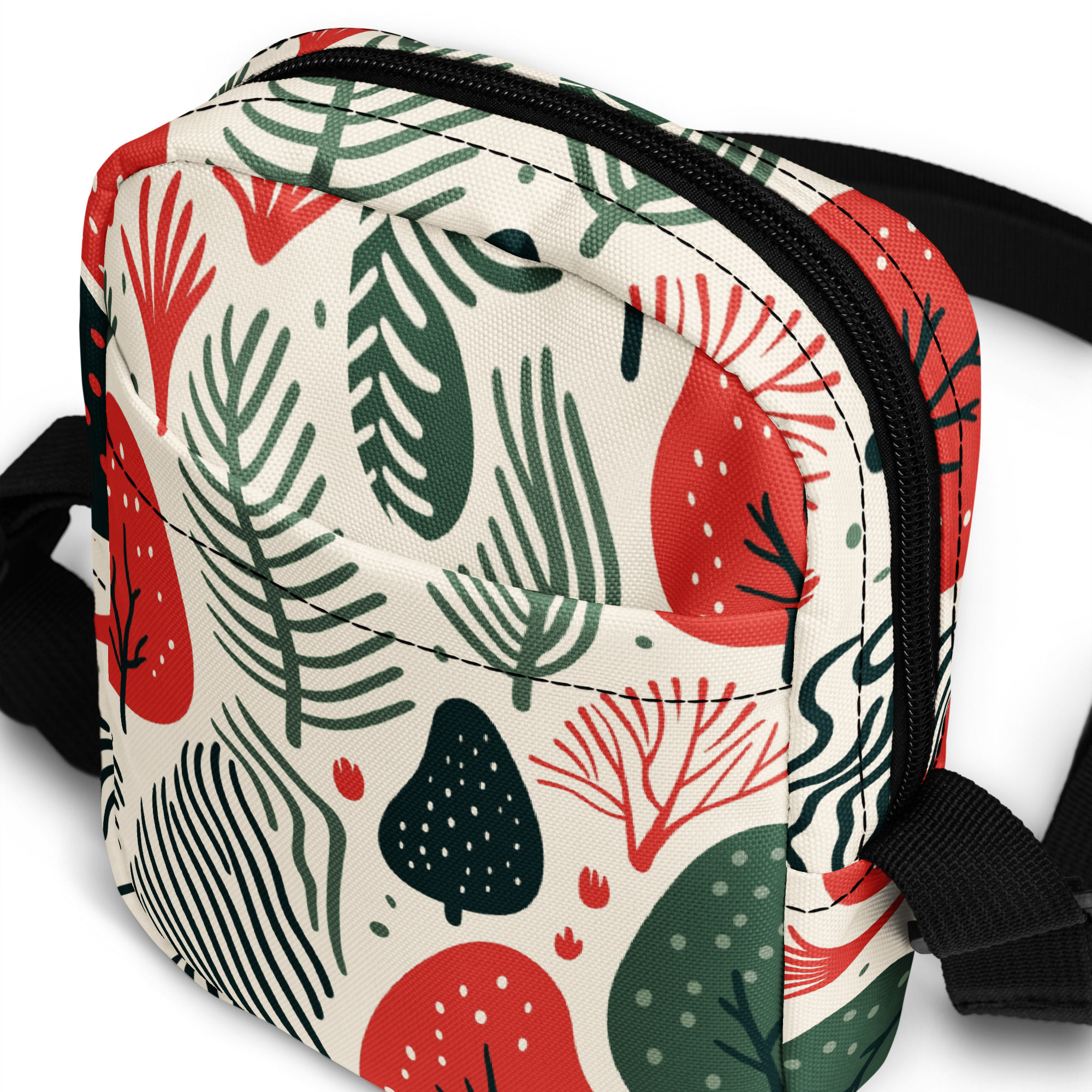 Cream crossbody sling bag with a bold pattern of red, green, and black abstract leaves, ferns, and dotted modern shapes.