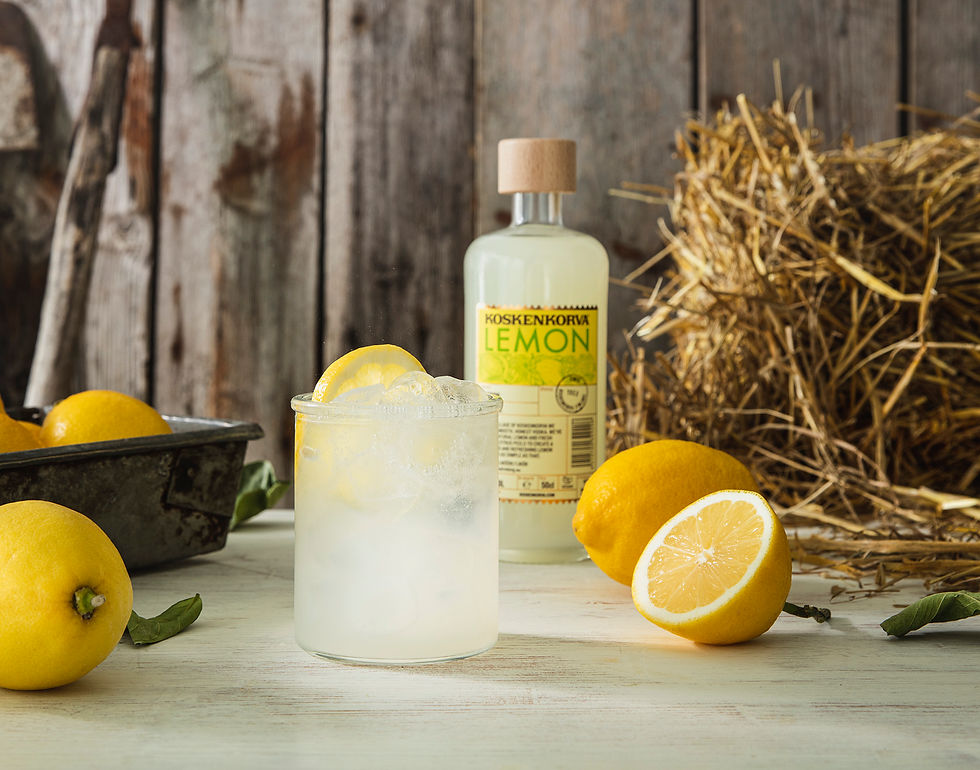 パッションフルーツリキュールが入ったグラスと瓶が中心。背景に果物と穀物。ラベルに「KOSKENKORVA PASSIONFRUIT」の文字。ナチュラルな雰囲気。