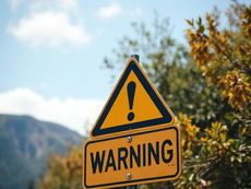Yellow triangular warning sign with exclamation mark in nature setting. Text reads "WARNING." Background includes trees and mountains.