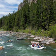White raft with people navigating a rocky river through pine forest and cliffs under a partly cloudy sky