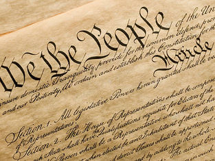 Close-up of the U.S. Constitution with "We the People" in bold, elegant script. The aged parchment adds a historical feel.