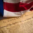 American flag draped over the Declaration of Independence document dated July 4, 1776. The flag's colors are vivid red, white, and blue.