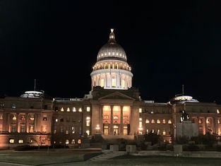 Illuminated capitol building at night with a prominent dome, warm lights glowing. Dark sky above enhances its grand architecture.