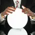 Man in a suit holds a glowing white crystal ball over a glossy black surface, creating a mysterious mood.