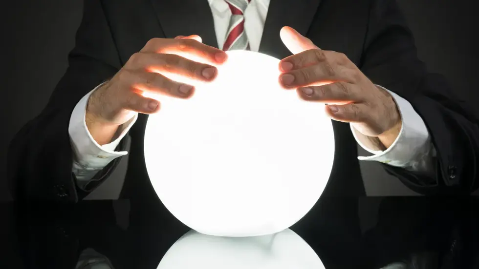 Man in a suit holds a glowing white crystal ball over a glossy black surface, creating a mysterious mood.