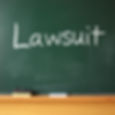 The word "Lawsuit" is written in white chalk on a green chalkboard with an eraser and books on a wooden ledge below.