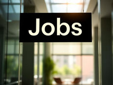 Black hanging sign reading Jobs in a bright glass office lobby with sunlight and blurred seating in the background.