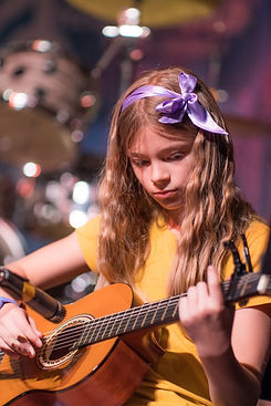 A young girl performing on her guitar at a music academy recital in Toronto