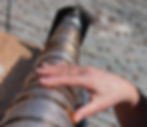 Hand wearing a ring touches glass discs on a street instrument. The scene is sunlit, creating a warm, reflective atmosphere. Stone pavement visible.