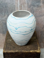 A curved wheel thrown white vase with carved lines around the body. Fired with a white glaze and wobbly stripes of blue glaze.