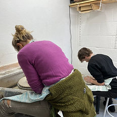 Back views of two people in a pottery lesson sat at potter's wheels throwing pots