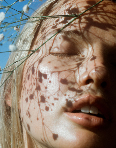 Close-up of a serene face bathed in sunlight, with delicate shadows of baby's breath flowers cast across the skin, evoking a soft and natural aesthetic.