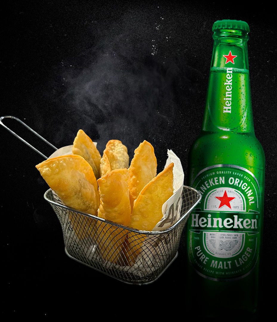 Cesta d pastel frito com fumaça ao lado de uma garrafa verde de cerveja Heineken, sobre fundo preto. Atmosfera apetitosa.