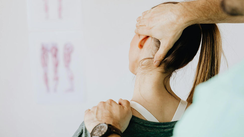 Back view of crop faceless bearded orthopedist in wristwatch checking up neck of anonymous lady while standing in front of wall with paper drawings representing body anatomy