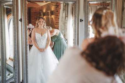 Bride Kate smiling at her reflection in wedding dress, Mythe Barn