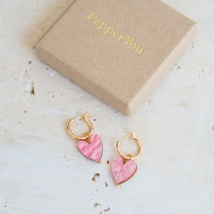 A romantic pair of gold hoop earrings with a dangling delicate light pink pearlescent acrylic charm