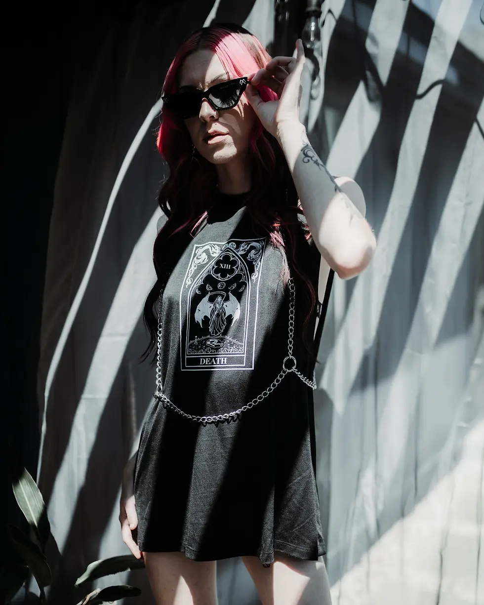 Thumbnail: An alternative woman wearing a gothic printed t-shirt dress has styled it with the pretty cults sacrifiant chain harness.