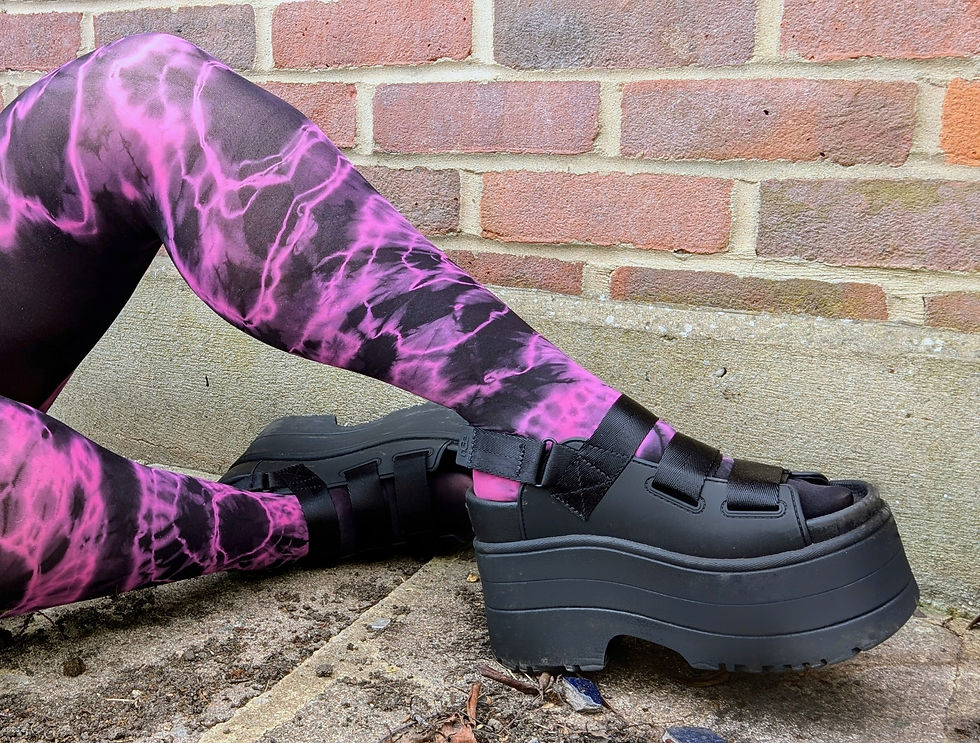 A pair of legs wears a gothic pair of tie dye tights in black and bright fuchsia pink styled with chunky black shoes.