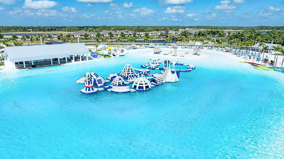 Large aqua park with people enjoying inflatable obstacle courses on bright blue water, surrounded by sandy shores and palm huts. Arial view.