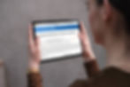 Woman holding a tablet displaying "News Release Details" about Sun Country Airlines' 2025 Q1 results. Plain gray background.