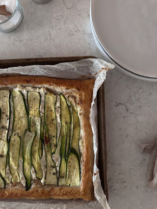 Golden puff pastry zucchini ricotta tart with thinly sliced zucchini, fresh herbs, and creamy ricotta on a parchment-lined baking tray