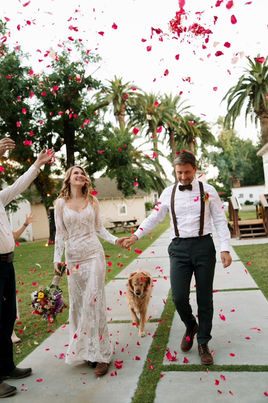  Bride and groom walking through a petal toss with their dog at an outdoor Central California ranch wedding.
