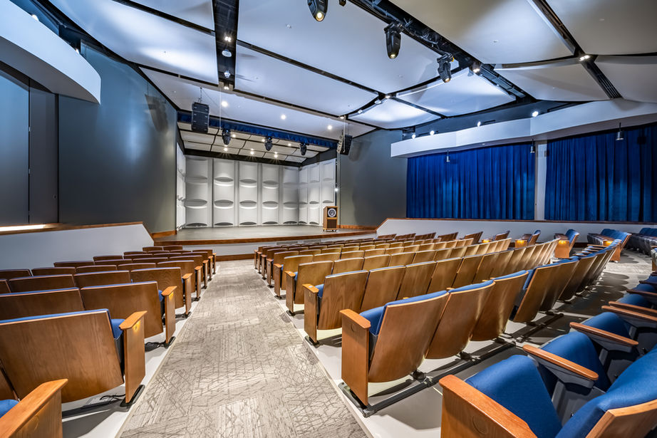 Other side view of auditorium with rows of seating and stage with blue curtains.