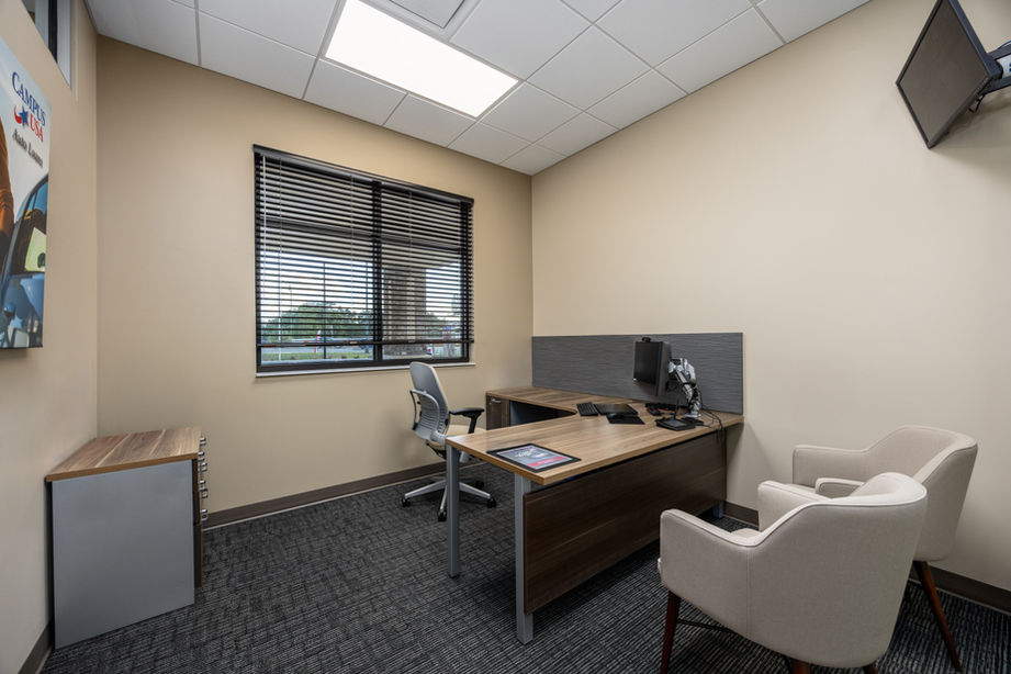 Modern office setup with desk, chairs, window, and computer in spacious room.