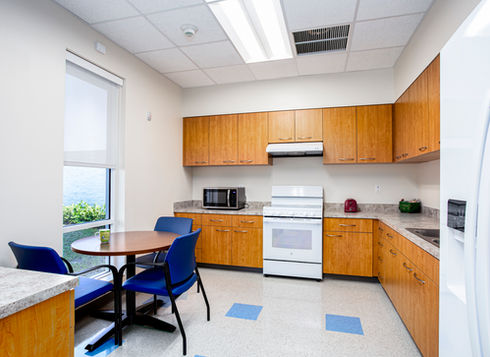 Modern breakroom kitchenette with wooden cabinets and blue chairs