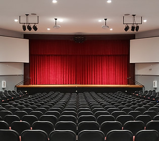 Santa Fe High School Auditorium elevated stage with red curtain, stage lighting, projection screens, and rows of auditorium seating