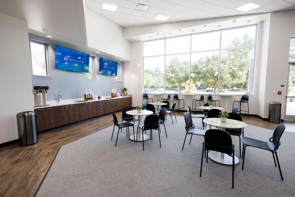 Multi-purpose hospitality and study space with tables, chairs, and large windows with trees outside.