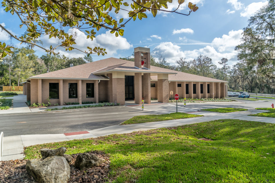 Exterior view of a beige building with columns, and a heart with a cross in it under a sunny sky.