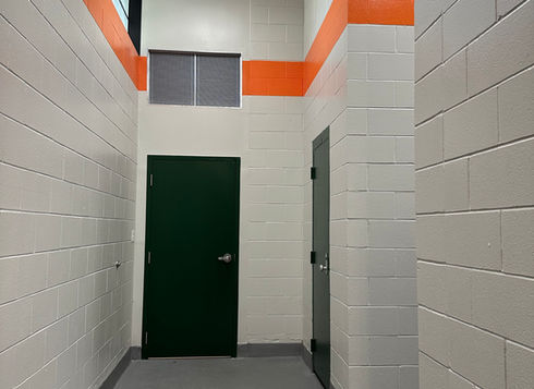 K-12 school hallway with and office door, white brick walls and orange stripe