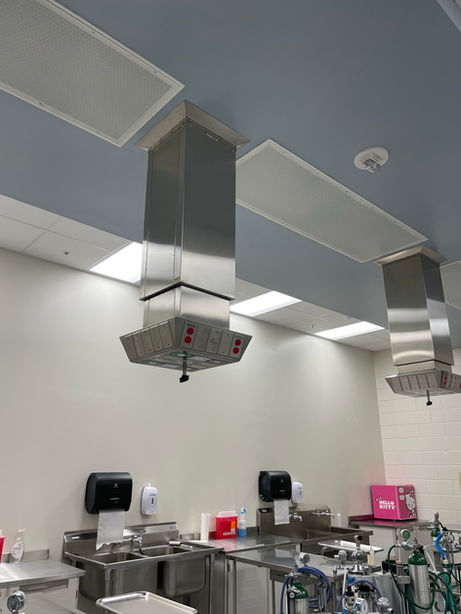 Zoomed in view of a stainless steel power supply and ventilation over an exam table in a laboratory setting with white walls.