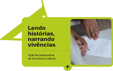 Botão retangular, na cor verde, com cantos arredondados e uma forma triangular vazada para fora no canto superior esquerdo. Texto à esquerda, imagem à direita. Texto: Lendo histórias, narrando vivências. Ação socioeducativa de incentivo à leitura. Imagem: mãos seguram caneta, papel escrito ao fundo