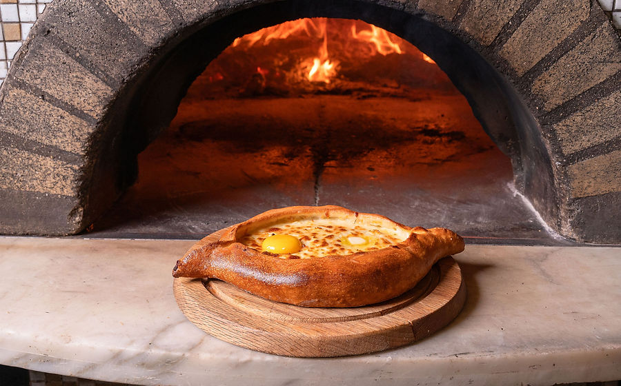 Khachapuri Adjaruli with butter and egg in front of Bevri's wood oven