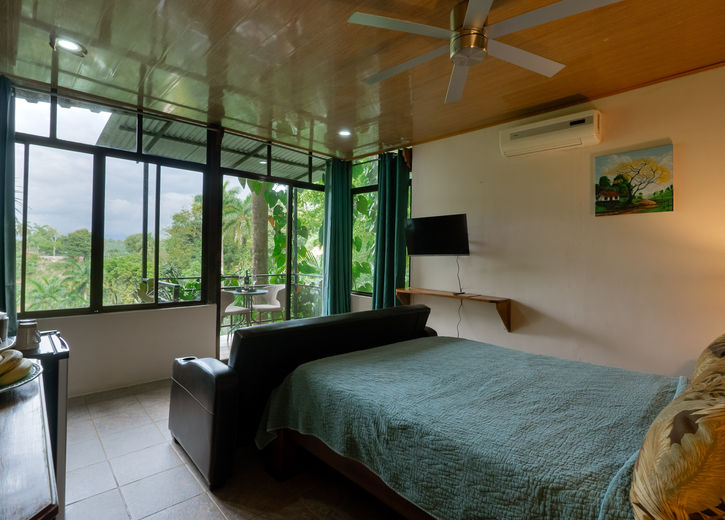 Bedroom with large windows, teal bedding, and jungle and mountain views in the Tree Top Canopy room at Boutique Hotel Las Cascadas