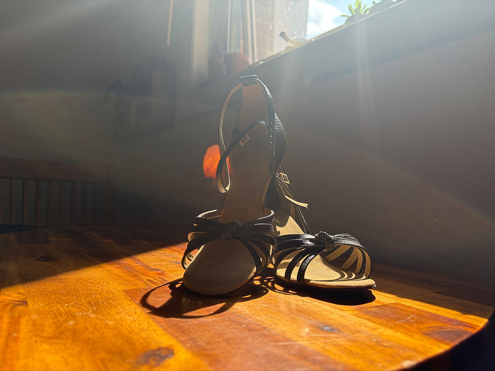 A pair of black dance shoes resting unworn on a wooden table in warm afternoon sunlight.