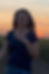 Woman in soft focus standing before a prairie sunset, an image of vulnerability, healing, and presence.
