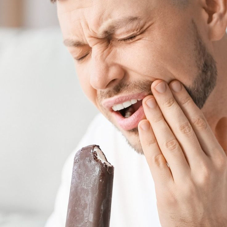 رجل يمسك بيده المثلجات في ألم ويمسك خده بيده الأخرى. يظهر تعبير وجهه الألم. الخلفية باهتة.