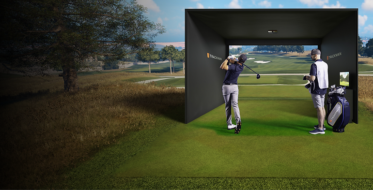 man is golfing in a finished swing pose, with a dark top, gray pants, and white shoes, in the foreground. Te background contains an image of a golf simulator screen where the image extends beyond what the golf simulator bay is to look like the simulator bay is on a golf course. View of a golf course.