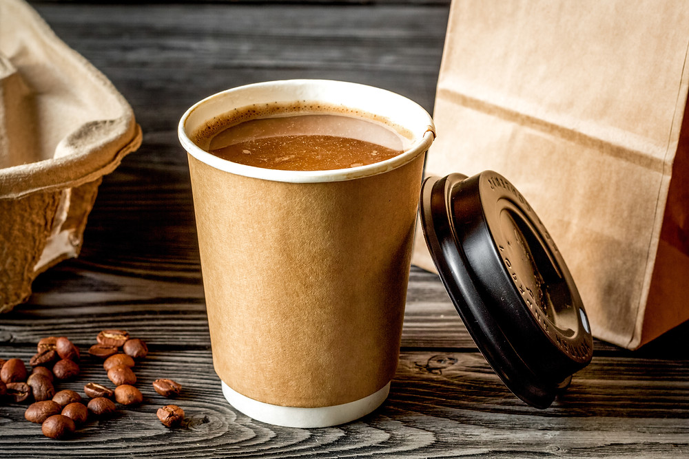 Coffee in a paper cup with coffee beans around it