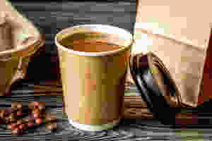 Coffee in a paper cup with coffee beans around it