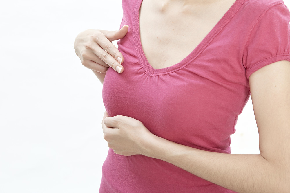 Woman in pink t-shirt checking herself for signs of breast cancer