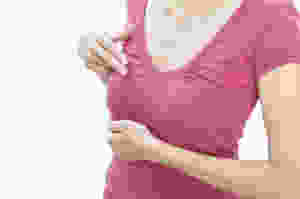 Woman in pink t-shirt checking herself for signs of breast cancer