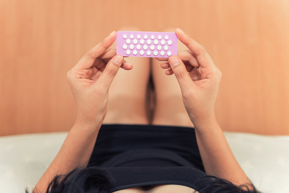 girl laying down and holding up hormonal birth control pills