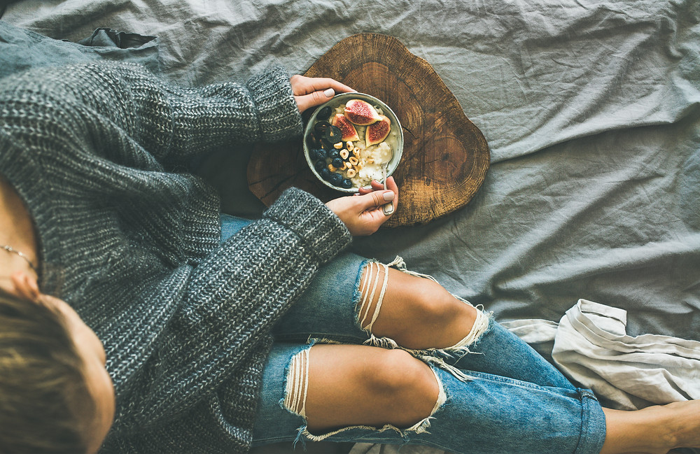 Girl in sweater and jeans sitting on her bed with something healthy
